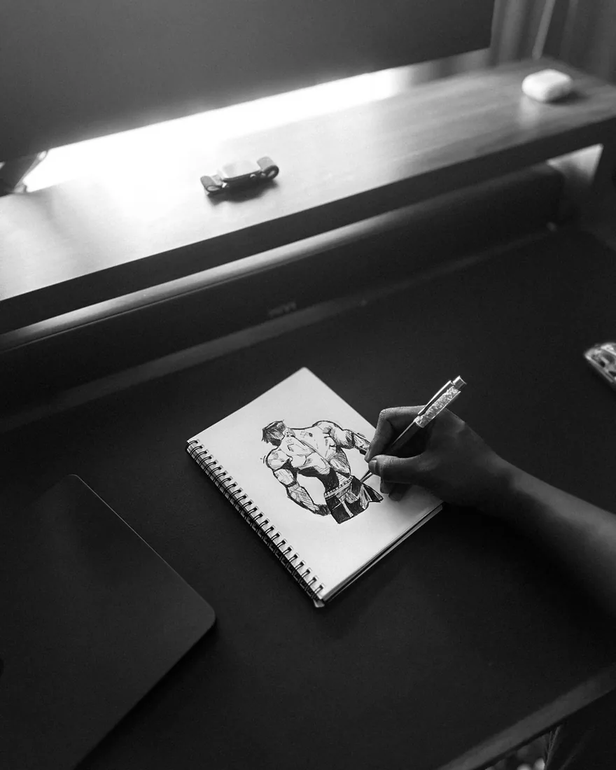Ruka kreslící komiksovou postavu tuší na papíře u pracovního stolu